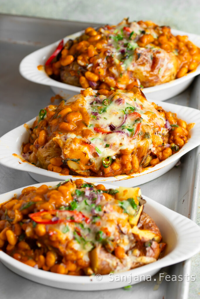 Jacket potato in a white dish topped with masala baked beans, melted cheese, chillies, onions and coriander.