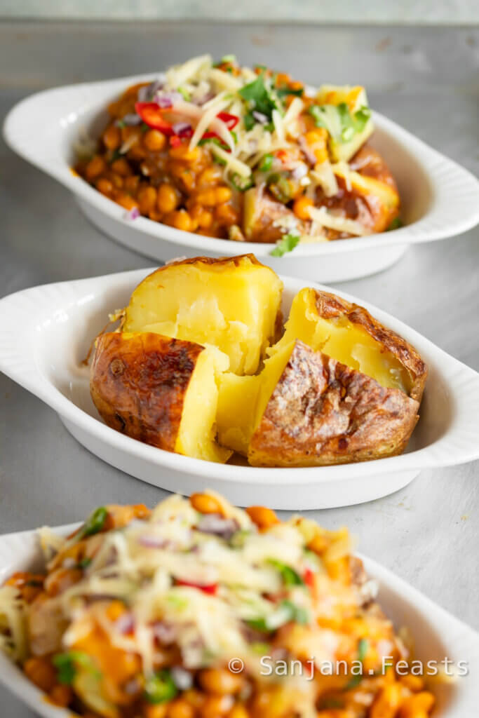 Jacket potato in a white dish topped with masala baked beans.